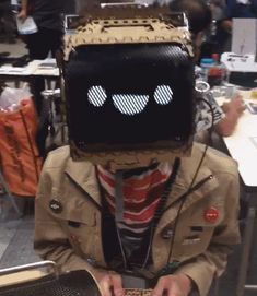 a person wearing a mask with eyes and head covering sitting in front of a table