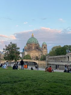 people are sitting on the grass in front of a large building with green dome tops