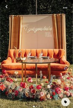 an orange couch sitting on top of a grass covered field next to a table with two glasses