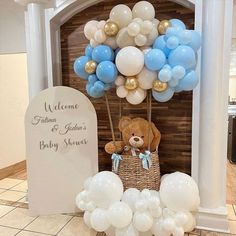 a teddy bear sitting on top of a basket next to balloons and a welcome sign