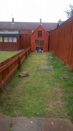 an empty yard in front of a red fence and wooden buildings with grass growing on the ground