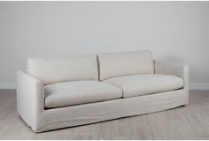 a white couch sitting on top of a hard wood floor next to a gray wall