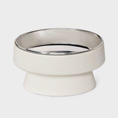 a white bowl sitting on top of a white pedestal with a silver ring around it