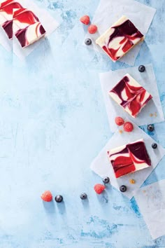 three slices of cheesecake with raspberries and blueberries on the side next to each other