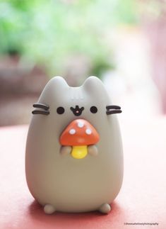 a small gray cat figurine sitting on top of a red table next to a green plant