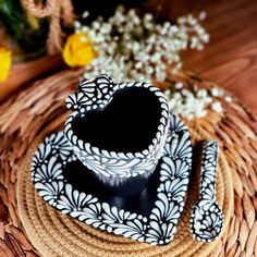 a black and white heart shaped cup sitting on top of a wicker place mat