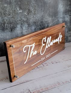 a wooden sign that says the ellwoods with white lettering on it, against a gray wall