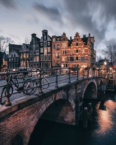 a bridge over a river with bicycles parked on it's sides and buildings in the background