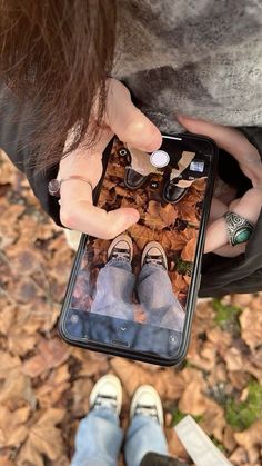 a person holding an iphone in their hands and looking at the screen with autumn leaves on it