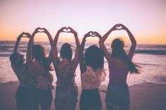 four girls making heart shapes with their hands on the beach at sunset or sunrise time