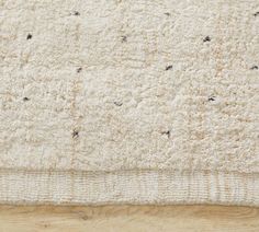 a white rug with tiny black dots on the top and bottom corner, laying on a wooden floor