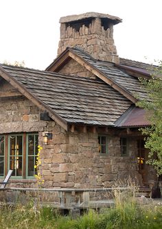 an old stone house with a chimney on the roof and windows in front of it