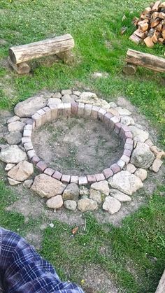 a fire pit sitting in the middle of a field next to some logs and grass