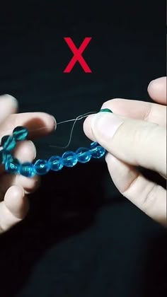 two hands are working on a piece of blue glass beaded wire with red x in the background