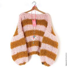 a pink and brown striped sweater hanging on a wooden hanger with a tag attached to it