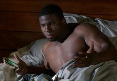 a shirtless man laying in bed holding a cell phone and pointing to the screen