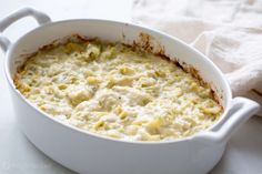 a white casserole dish filled with cheese and sauce on top of a table