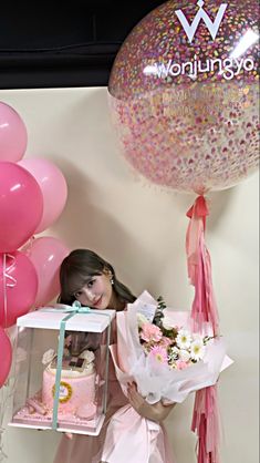 a woman is holding a box with flowers and cake in it while standing next to balloons