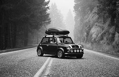 a black and white photo of a small car with a surfboard on the roof