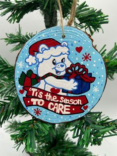 a christmas ornament hanging from a tree with a teddy bear holding a present