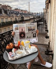 a person sitting at a table with a tray of food on it while reading a newspaper