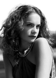 black and white photograph of a woman with long curly hair sitting on the ground, looking at the camera