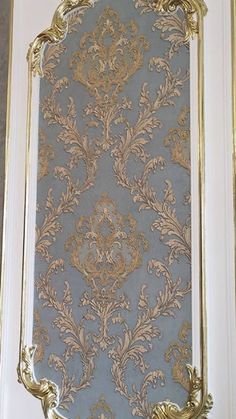 an ornate gold and blue wallpaper in a room with white trim on the walls