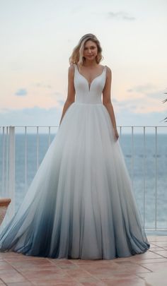 a woman in a white and blue wedding dress standing on a balcony overlooking the ocean