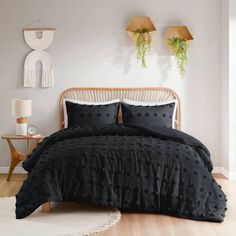 a bed with black bedspread and pillows in a white room next to two plants