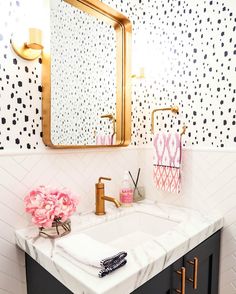 a bathroom with black and white wallpaper, gold fixtures and a mirror above the sink