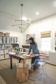 a woman sitting at a table in a room with lots of shelves and baskets on the floor