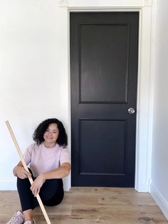 a woman sitting on the floor with a broom in front of her and a black door behind her