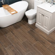 a white bath tub sitting next to a toilet in a bathroom on top of a wooden floor