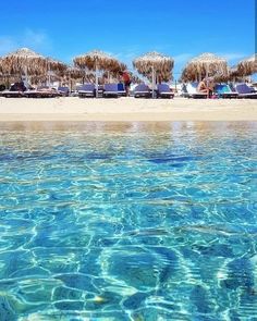 umbrellas and lounge chairs on the beach in clear blue water, near an ocean