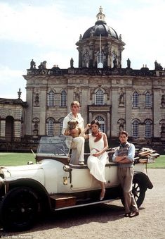 three people are sitting on top of an old car in front of a large building