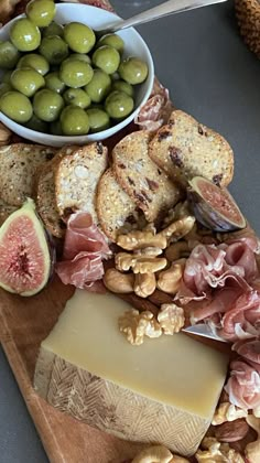 an assortment of cheeses, meats and olives on a wooden platter