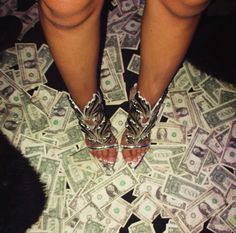 a person standing on top of a pile of money wearing high heeled shoes and silver heels