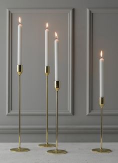 three white candles are lined up next to each other on a table in front of a gray wall