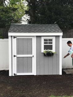 a man standing next to a shed with a window on the side and a potted plant in it