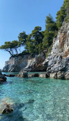 the water is crystal blue and clear with rocks on both sides, and trees in the background