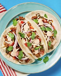 three tacos with meat, onions and cilantro on a plate next to a striped napkin