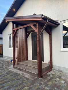 a wooden gazebo sitting on the side of a house next to a brick walkway