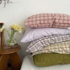 a stack of pillows sitting on top of a bed next to a vase with flowers