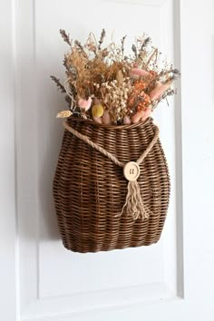 a wicker basket with dried flowers hanging on the front door hanger for decoration