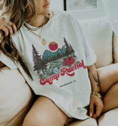 a woman sitting on top of a white couch wearing a shirt that says camp ranch