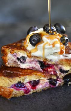 two pieces of french toast with blueberries and whipped cream on top are being drizzled with syrup