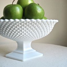 a white bowl filled with green apples on top of a table