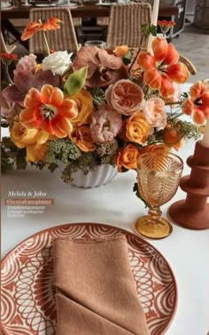 an arrangement of flowers in a vase on a dining room table with place settings and napkins