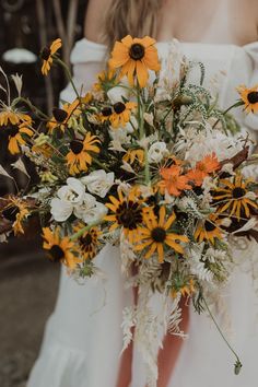 a bride holding a bouquet of sunflowers and other flowers in her hands,