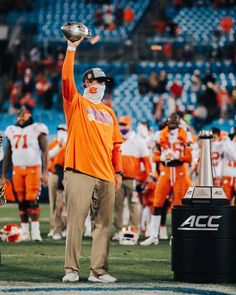 an orange and white football player wearing a face mask holds up a silver ball in the air